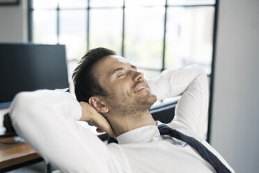 Smiling businessman in office leaning back - SBOF01574