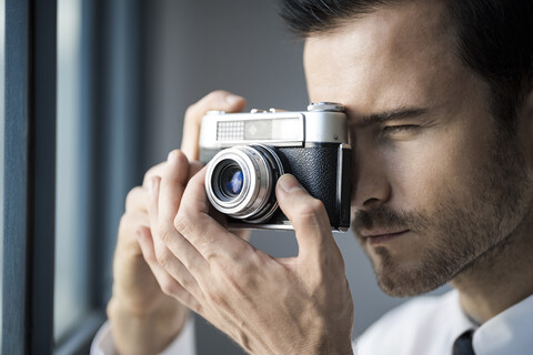 Nahaufnahme eines Geschäftsmannes, der ein Foto mit einer Retro-Kamera vor einem Bürofenster macht, lizenzfreies Stockfoto