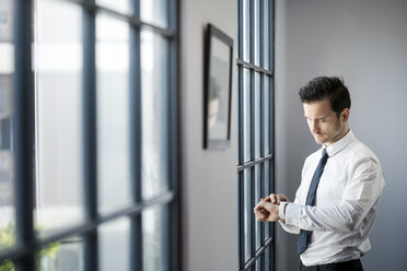 Geschäftsmann überprüft seine Smartwatch vor einem großen Bürofenster - SBOF01577