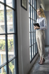 Selbstbewusste Geschäftsfrau mit Tablet im Büro stehend und aus dem Fenster schauend - SBOF01584