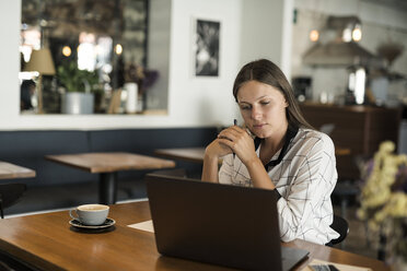 Young businesswoman in a cafe working with laptop on wooden table - SBOF01587