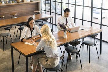 Colleagues discussing and working on laptop on wooden table in cafe - SBOF01592