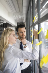 Kollegen schreiben auf gelbe Post-its am Fenster im Büro - SBOF01601