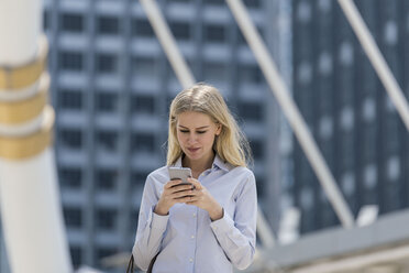 Blond woman with handbag checking cell phone in the city - SBOF01618