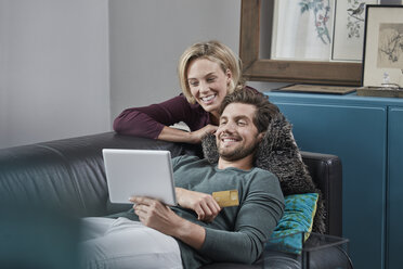 Happy couple with tablet on couch at home - RORF01579