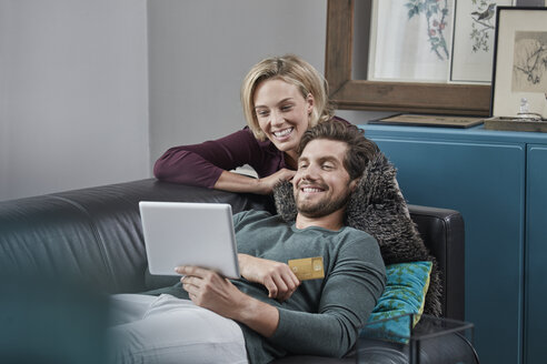 Glückliches Paar mit Tablet auf der Couch zu Hause - RORF01579