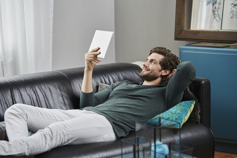 Lächelnder Mann mit Tablet, der zu Hause auf der Couch liegt, lizenzfreies Stockfoto