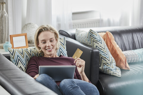 Glückliche Frau mit Tablet und Kreditkarte zu Hause auf der Couch liegend, lizenzfreies Stockfoto