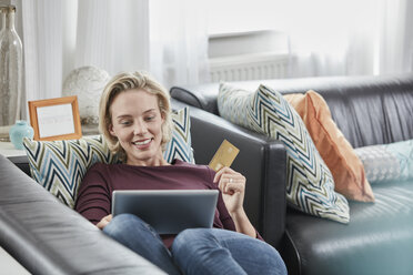 Happy woman with tablet and credit card lying on couch at home - RORF01584