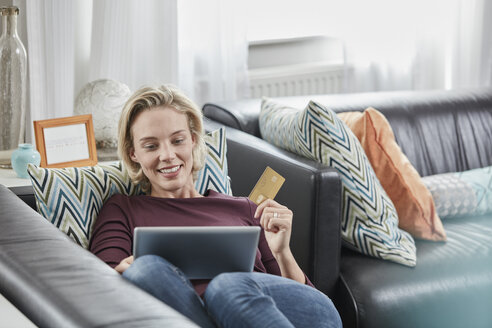 Glückliche Frau mit Tablet und Kreditkarte zu Hause auf der Couch liegend - RORF01584