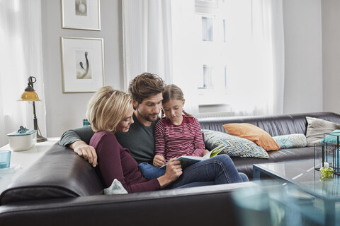 Familie sitzt zu Hause auf der Couch und liest gemeinsam ein Buch, lizenzfreies Stockfoto