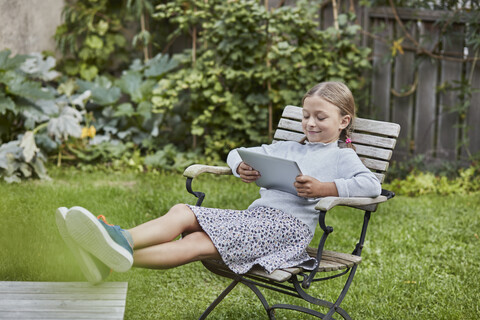 Lächelndes Mädchen benutzt Tablet im Garten, lizenzfreies Stockfoto