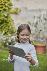Lächelndes Mädchen benutzt Tablet im Garten - RORF01597