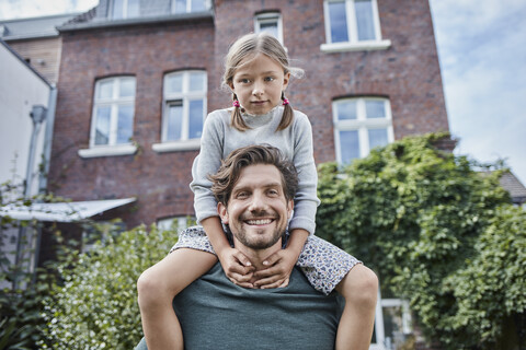 Porträt eines glücklichen Vaters mit Tochter im Garten ihres Hauses, lizenzfreies Stockfoto