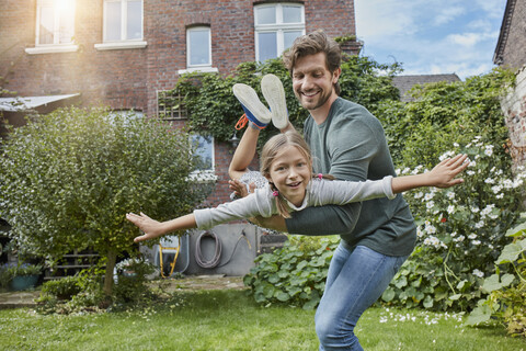 Glücklicher Vater spielt mit seiner Tochter im Garten ihres Hauses, lizenzfreies Stockfoto