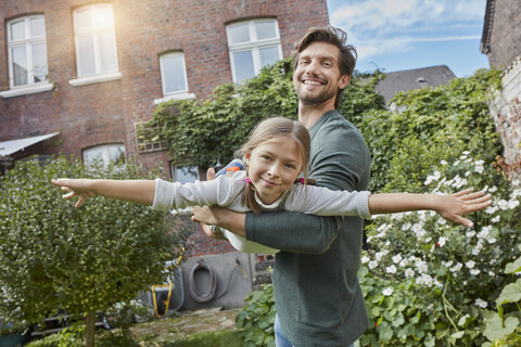 Glücklicher Vater spielt mit seiner Tochter im Garten ihres Hauses, lizenzfreies Stockfoto