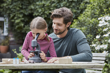 Vater und Tochter benutzen gemeinsam ein Mikroskop am Gartentisch - RORF01607