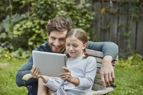Glücklicher Vater und Tochter benutzen gemeinsam ein Tablet im Garten, lizenzfreies Stockfoto