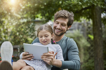 Glücklicher Vater und Tochter benutzen gemeinsam ein Tablet im Garten - RORF01610