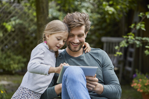 Glücklicher Vater und Tochter benutzen gemeinsam ein Tablet im Garten - RORF01612