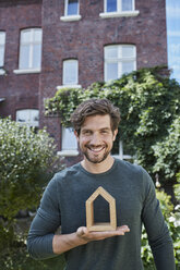 Portrait of smiling man in front of his home holding house model - RORF01614