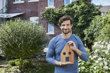 Portrait of smiling man in front of his home holding house model - RORF01618