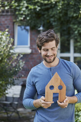 Portrait of smiling man in front of his home holding house model - RORF01619