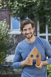 Portrait of smiling man in front of his home holding house model - RORF01620