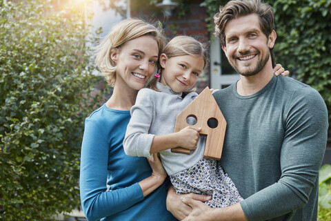 Porträt einer glücklichen Familie vor ihrem Haus mit Hausmodell, lizenzfreies Stockfoto