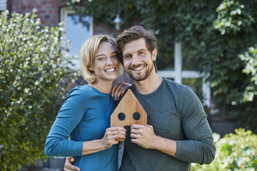 Porträt eines glücklichen Paares vor ihrem Haus mit Hausmodell - RORF01626