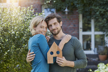 Porträt eines glücklichen Paares vor ihrem Haus mit Hausmodell - RORF01628