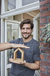 Portrait of smiling man at house entrance holding house model - RORF01635