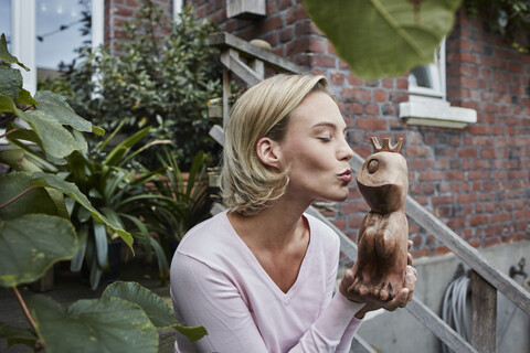 Young woman sitting on stairs kissing wooden frog prince stock photo