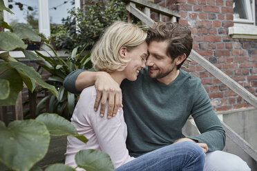 Happy couple sitting on stairs cuddling - RORF01650