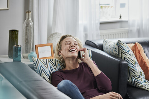 Laughing young woman on cell phone lying on couch at home stock photo