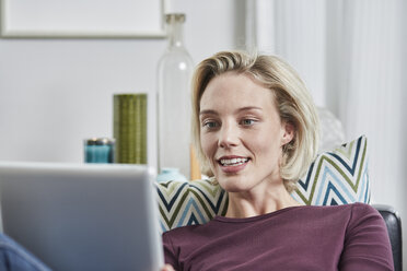 Junge Frau mit Tablet auf der Couch zu Hause liegend - RORF01661