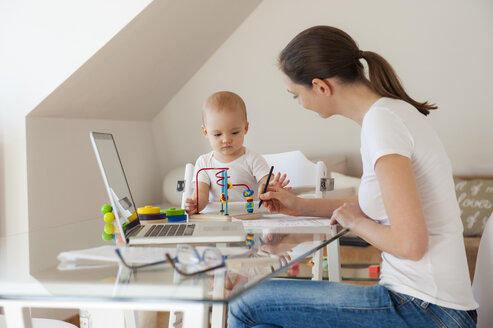 Mutter mit Laptop und kleine Tochter spielt am Tisch zu Hause - DIGF05614
