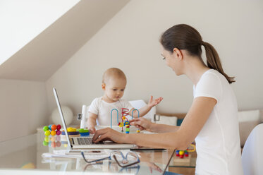 Mutter mit Laptop und kleine Tochter spielt am Tisch zu Hause - DIGF05615