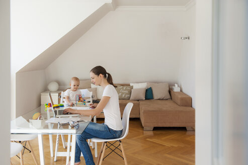Mutter mit Laptop und kleine Tochter spielt am Tisch zu Hause - DIGF05616