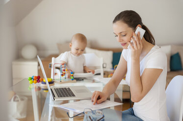 Mutter arbeitet und kleine Tochter spielt zu Hause am Tisch - DIGF05619