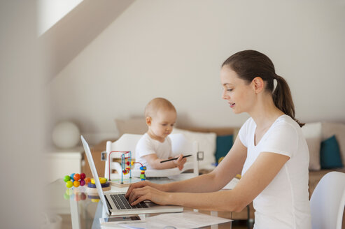 Mutter mit Laptop und kleine Tochter spielt am Tisch zu Hause - DIGF05620