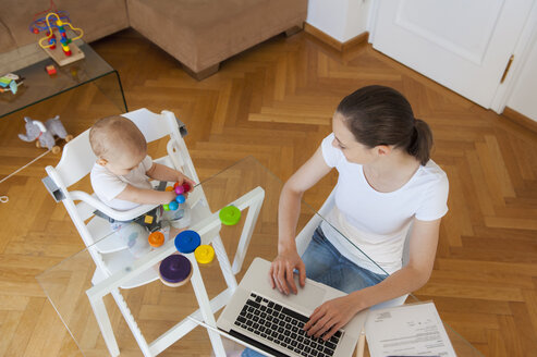 Draufsicht auf die Mutter, die einen Laptop benutzt, und die kleine Tochter, die zu Hause am Tisch spielt - DIGF05623