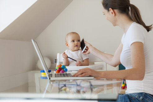 Mutter arbeitet mit kleiner Tochter, die zu Hause am Tisch spielt - DIGF05627