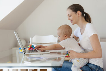 Lächelnde Mutter und kleine Tochter benutzen gemeinsam einen Laptop am Tisch zu Hause - DIGF05628