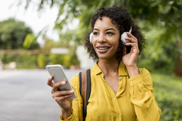 Porträt einer lächelnden Frau, die mit Kopfhörern und Smartphone im Freien Musik hört - MAUF02341