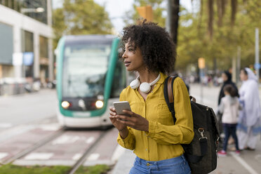 Frau mit Rucksack und Kopfhörern bei der Nutzung eines Smartphones in der Stadt - MAUF02355