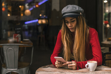 Porträt einer jungen Frau, die auf der Terrasse eines Cafés eine SMS schreibt - ACPF00370