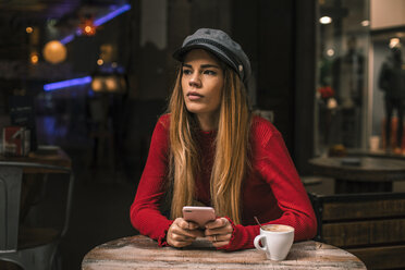 Porträt einer nachdenklichen jungen Frau mit Smartphone auf der Terrasse eines Cafés - ACPF00371