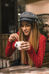 Porträt einer lächelnden jungen Frau, die auf der Terrasse eines Cafés sitzt und Kaffee umrührt - ACPF00374