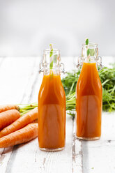 Carrots, glasses of carrot juice and swing top bottles on wood - LVF07660